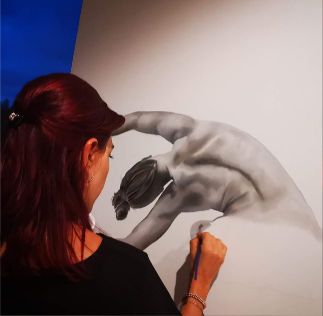 Artista pintando una figura monocromática sobre un muro claro.